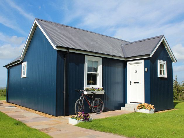 blue clad small house white window frames white door planter with flowers red bike