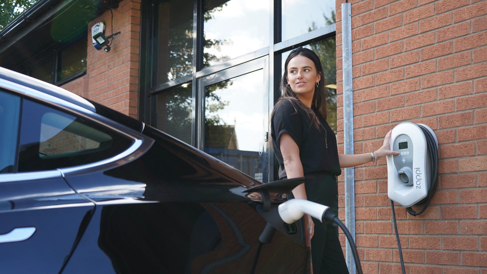 A woman using a MyEnergi Zappi to charge a dark-coloured Tesla