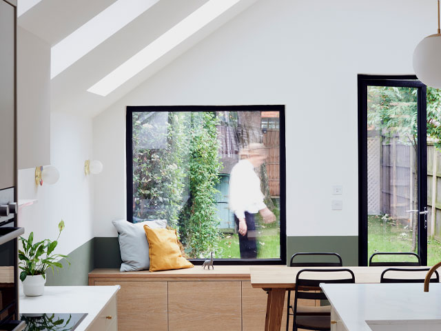 pitched roof kitchen extension with white walls, black-framed windows and natural wood storage bench under the picture window