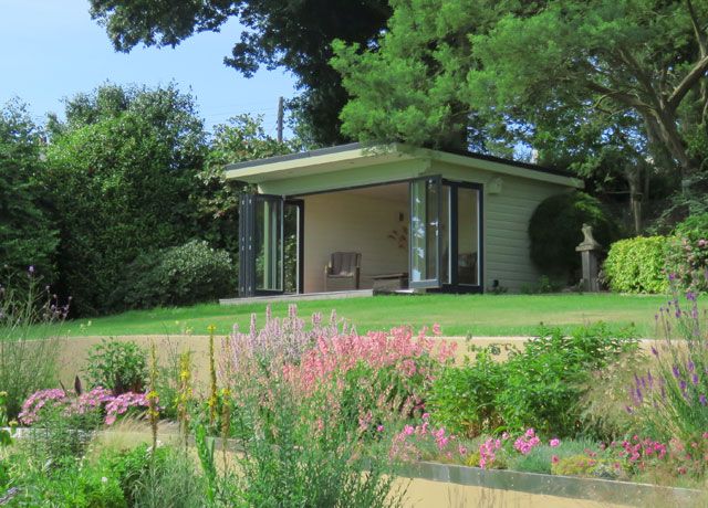 A Scandi-style garden room in an outdoor space with lots of greenery and pink flowers by Norwegian Log Extensions