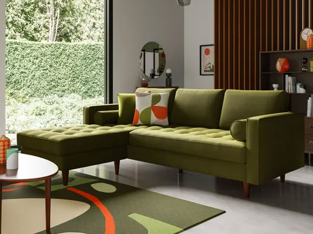 retro green couch with chaise in a living room with orange accessories and wooden wall panelling 